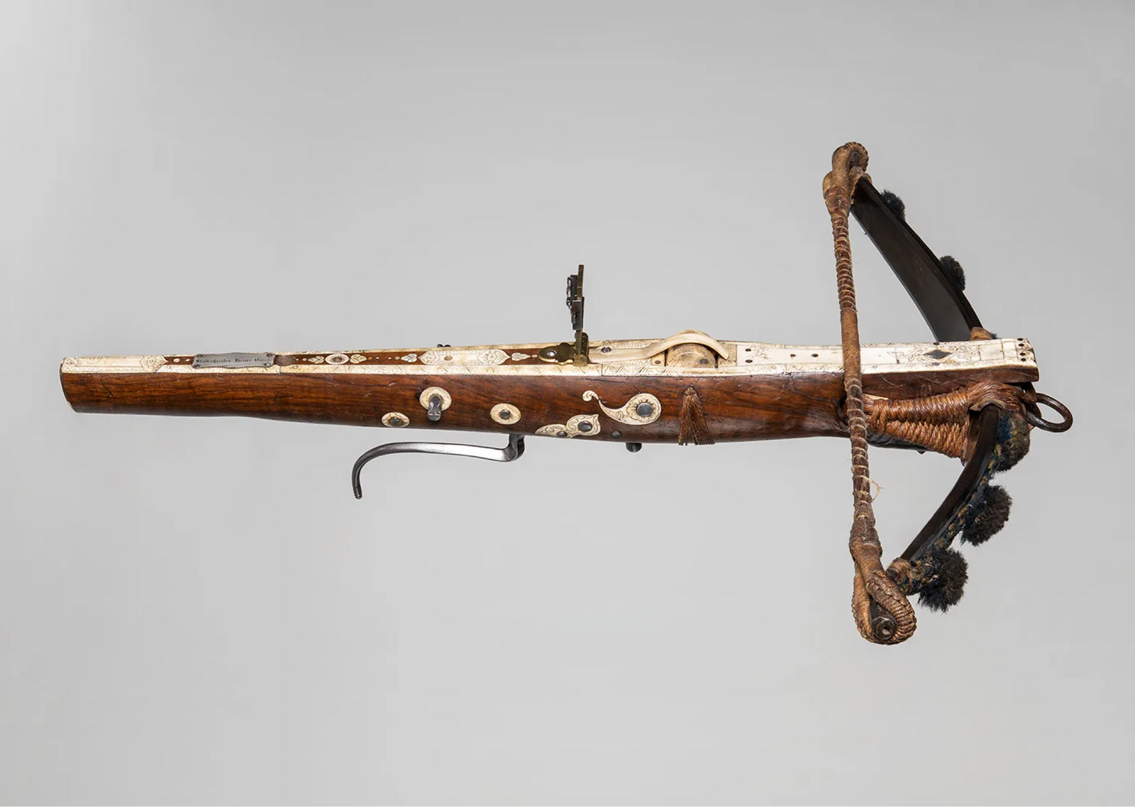 An antique historical crossbow with a carved wooden stock, intricate bone inlay decorations, metal sight, and steel bow.