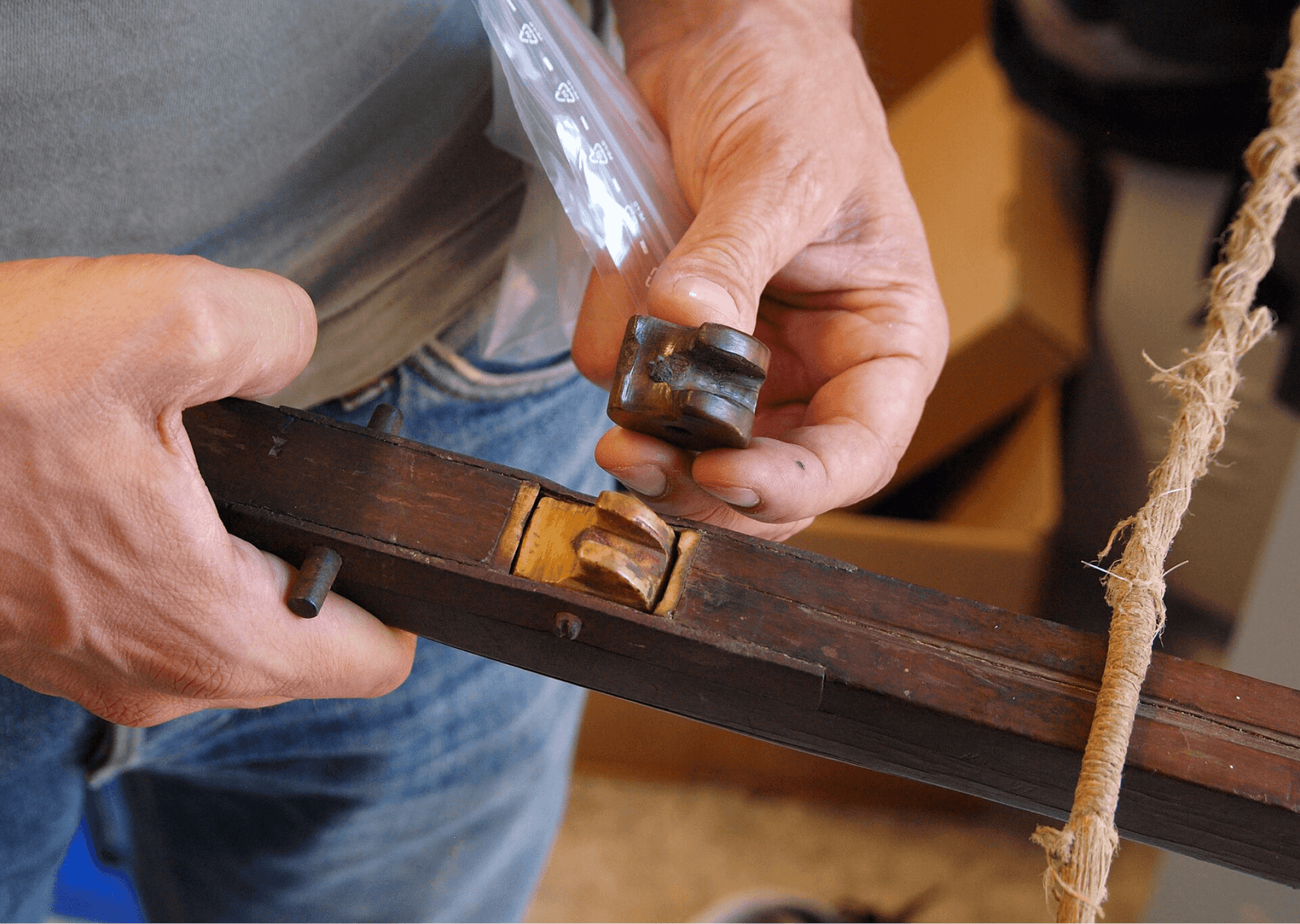 A person holding a wooden crossbow stock and demonstrating the installation of a historic trigger rolling nut mechanism.