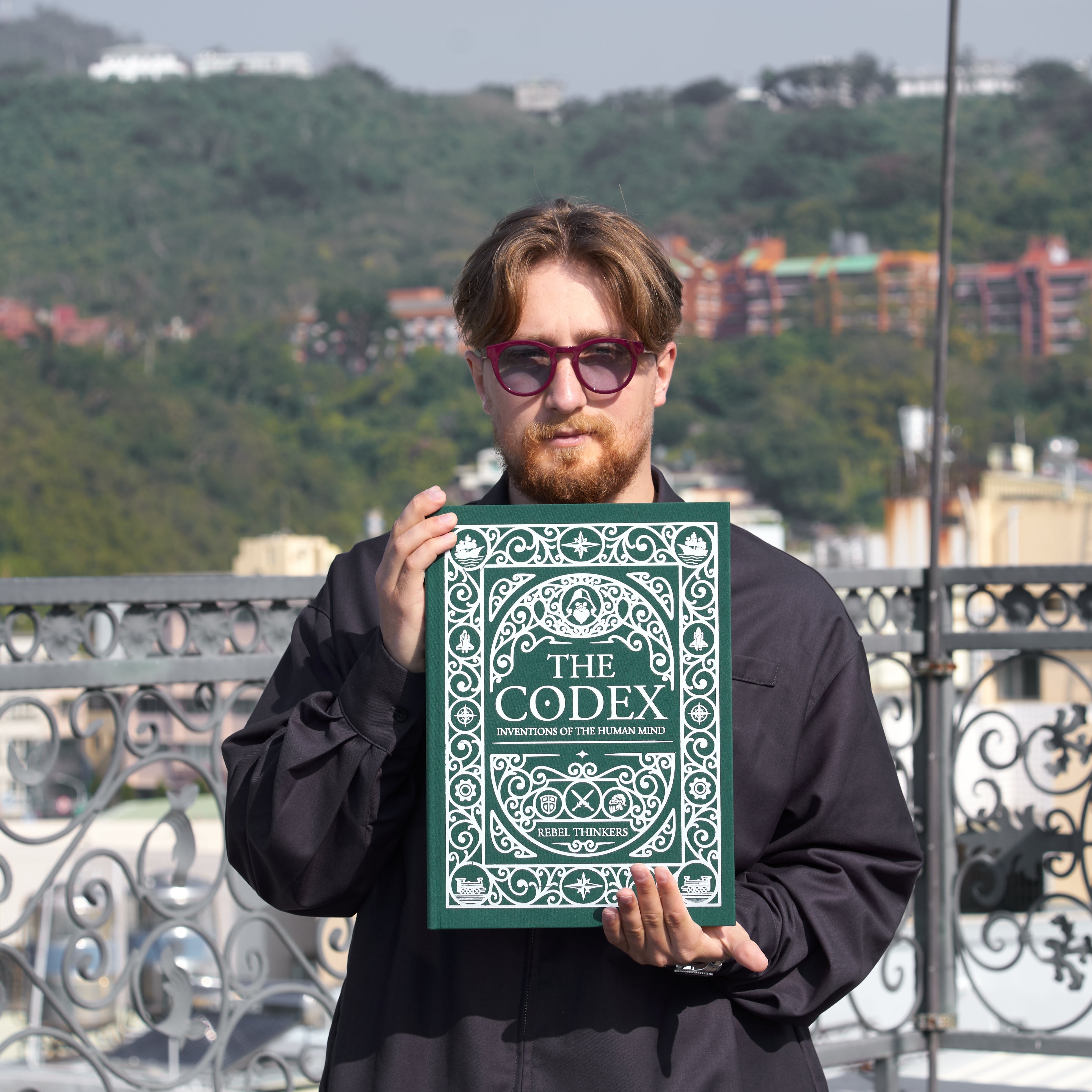 A person holding a book titled 'The Codex: Inventions of the Human Mind. How the World Works' with a green cover featuring illustrations of human heads and scientific symbols.