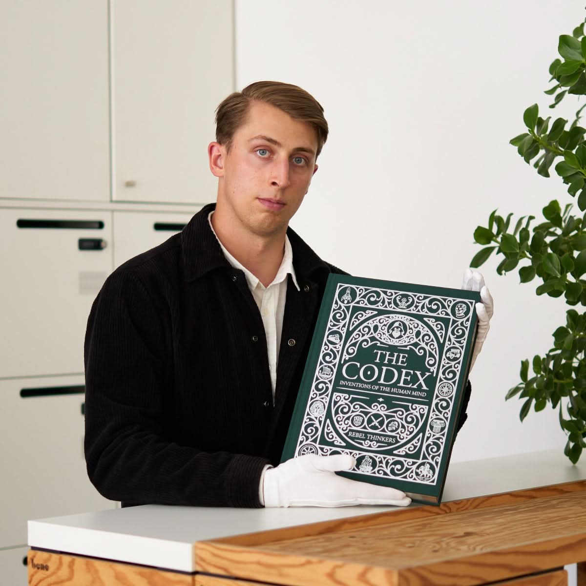 Man holding The Codex Book of inventions , a large illustrated kids encyclopedia of inventions in Da Vinci-inspired style, showing its size and ornate green cover.