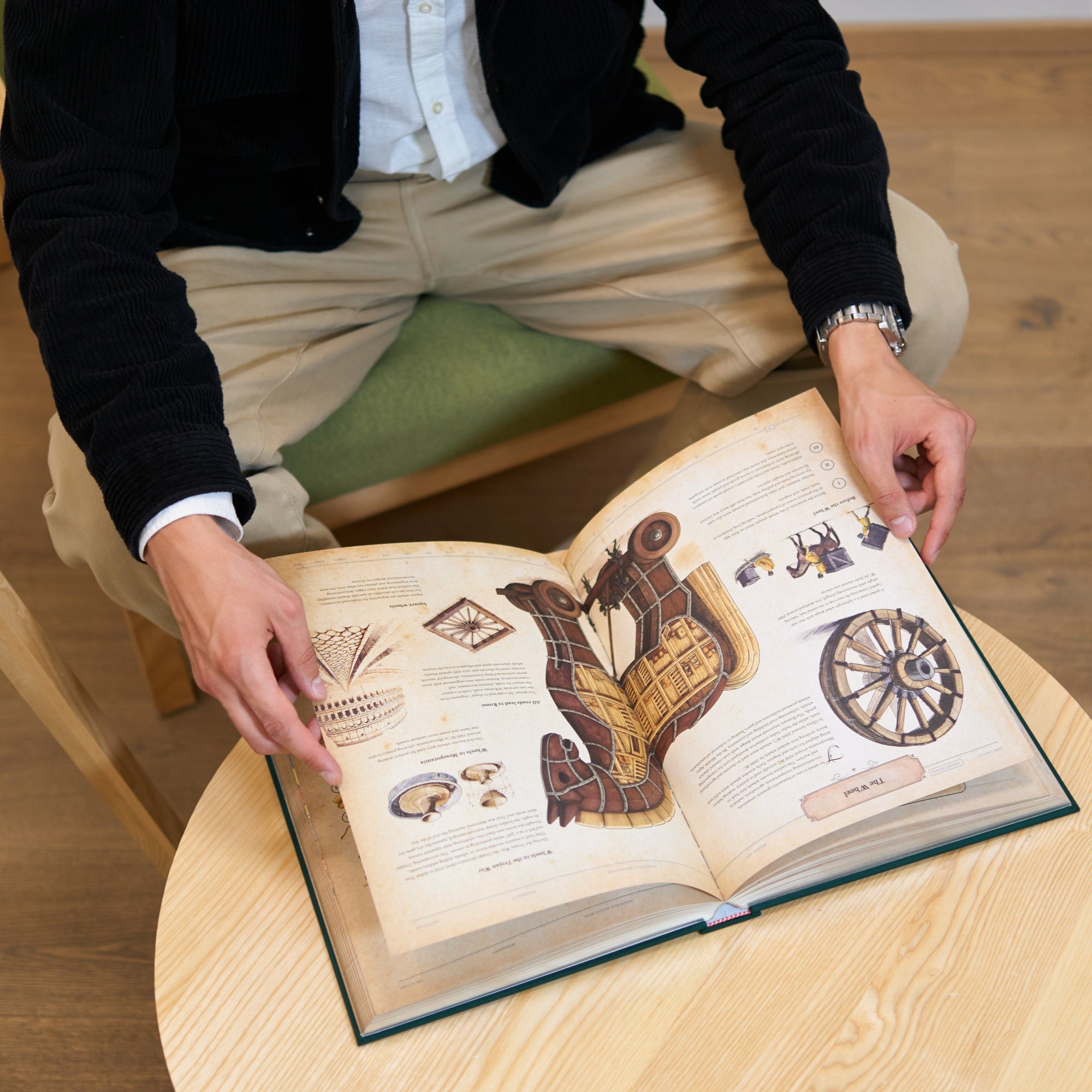 Open pages of The Codex showing illustrated history of wheel-based inventions and engineering mechanisms, displayed on a wooden coffee table in use