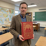 Man holding a book titled 'The Codex' in a classroom setting