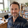 Portrait of a smiling middle-aged man with a short beard in a striped shirt sitting in his home office.