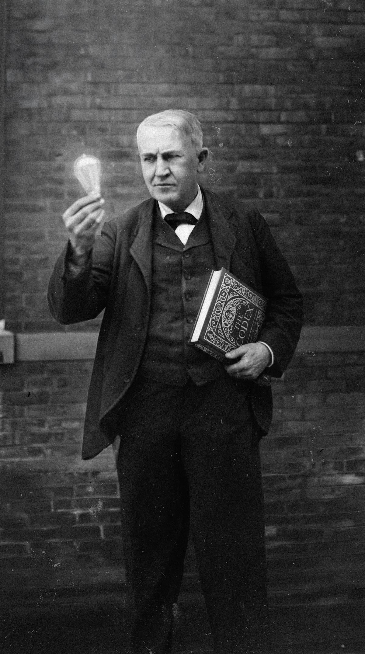 Black-and-white image of Thomas Edison holding The Codex: Inventions of the Human Mind illustrated book, connecting invention history, technology, and great thinkers