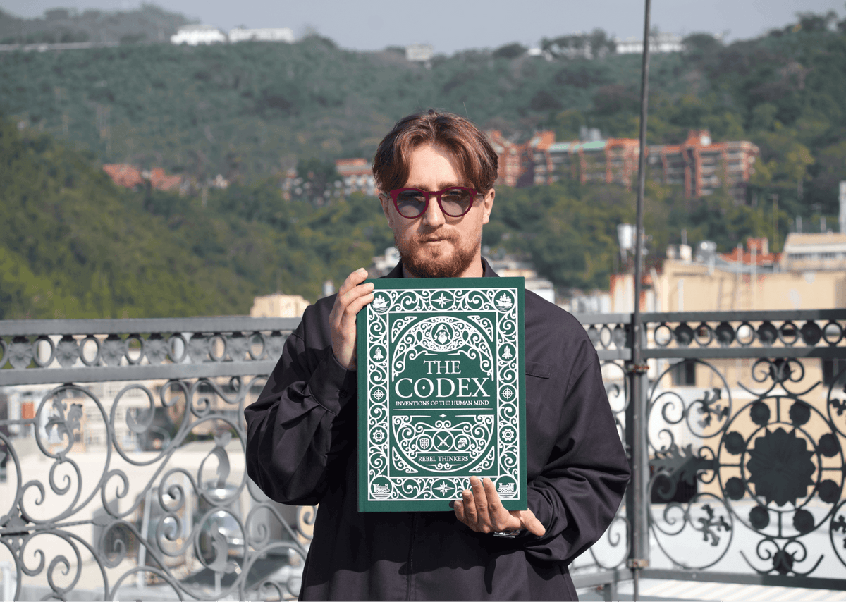 Front cover of The Codex book held by a young man outdoors with hills in the background.