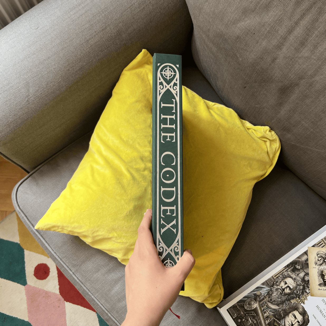 A hand holding the decorated spine of The Codex hardcover book volume.